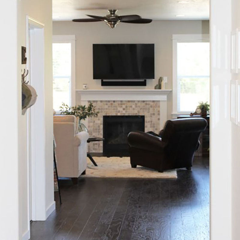 View from a hallway looking into a living room with dark laminate flooring, a plush beige area rug, and a fireplace with a tile design on the front, all from Standard Paint & Flooring.
