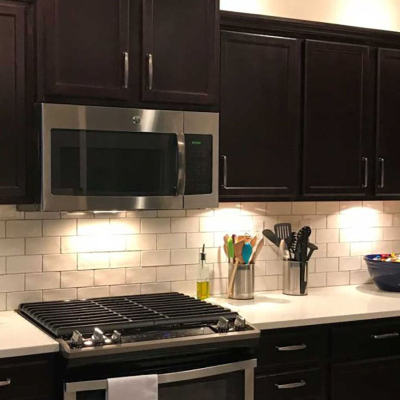 Dark wooden kitchen cabinets with white subway tile backsplash from Standard Paint & Flooring and a stainless steel stove and microwave above the stove.