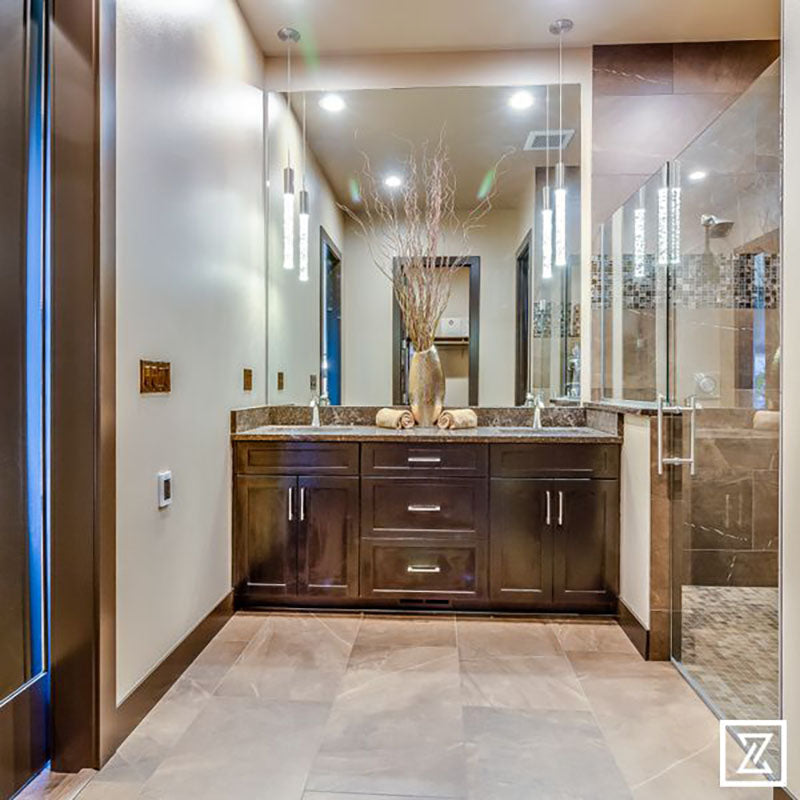 A bathroom with dark brown cabinets, marble countertop and large mirror, with light brown ceramic tile from Standard Paint & Flooring.