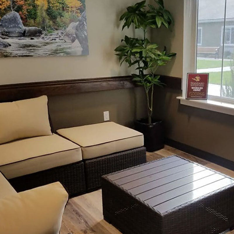 A waiting room with a couch with large beige cushions and new laminate flooring by Standard Paint & Flooring.