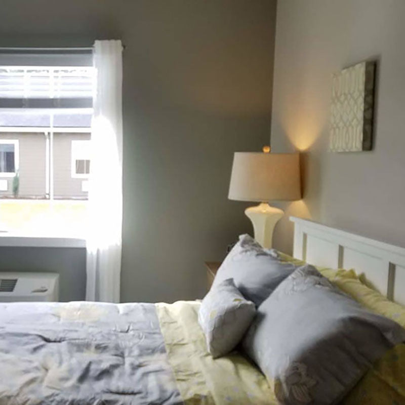 A bedroom painted grey with paint from Standard Paint & Flooring, with a bed with grey and yellow blankets and pillows.