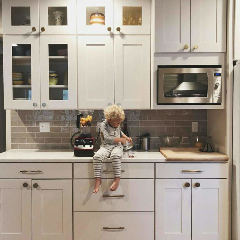 White kitchen cabinets from Standard Paint & Flooring with a light brown back splash tile and a young child sitting on the kitchen counter.
