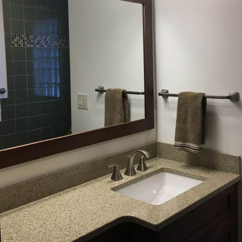 A renovated granite bathroom countertop and mirror with dark wooden trim, by Standard Paint & Flooring. 