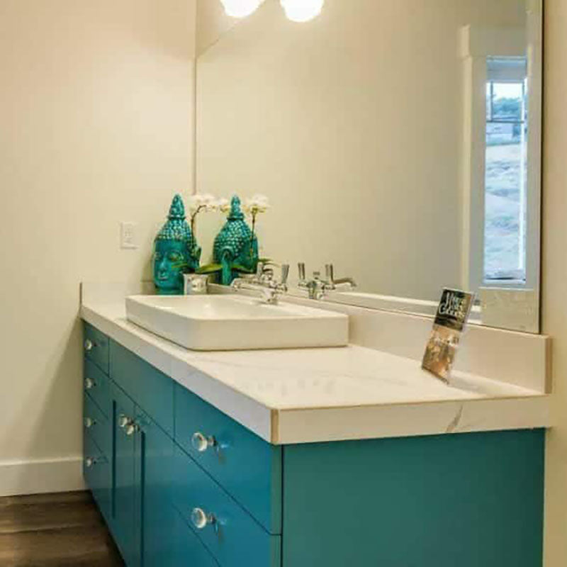 A bathroom vanity with turquoise cabinets by Standard Paint & Flooring, with a white marble countertop and white porcelain sink above the counter.
