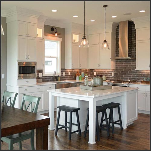 A kitchen with white cabinets, a white island with black stools, dark hardwood flooring and dark grey subway tile for a backsplash.