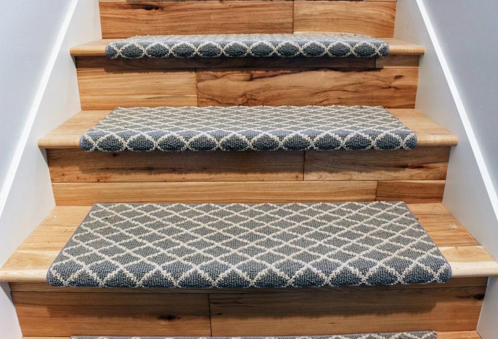 Light brown wooden staircase with a blue and white diamond printed carpet down the middle.
