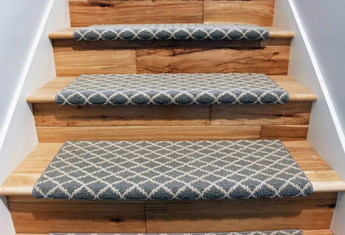 Light brown wooden staircase with a blue and white diamond printed carpet down the middle.