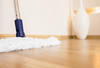 A white microfiber mop cleaning light colored hardwood flooring.