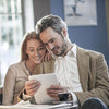 A woman and a man smiling as they look over a white tablet device.