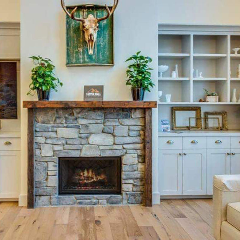A fireplace with natural large stones, with white cabinets and natural hardwood flooring by Standard Paint & Flooring.