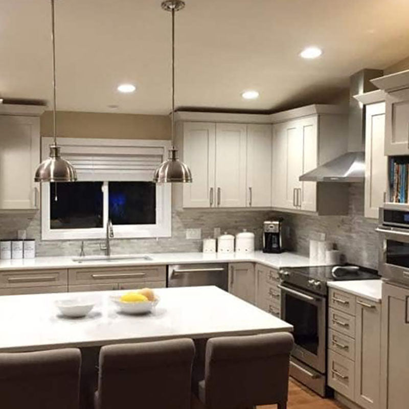 A kitchen with white cabinets and light grey backsplash tile from Standard Paint & Flooring, stainless steel appliances and an island with a white top. 