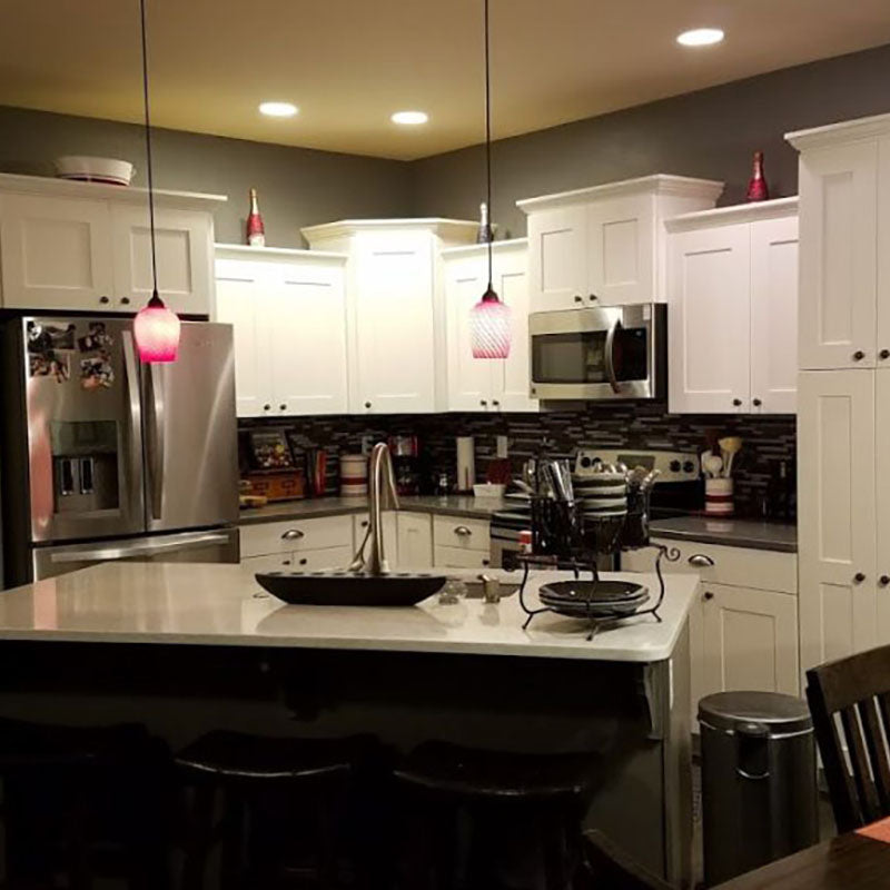 A kitchen with white cabinets and dark accent backsplash tile and hanging light fixtures from Standard Paint & Flooring, with a stainless steel fridge, stove and microwave.