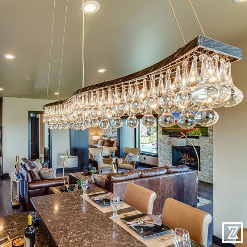 View from above a kitchen island with a granite countertop, light brown leather chairs and a large hanging light fixture, all designed by Kate Loeb, Designer at Standard Paint & Flooring. 