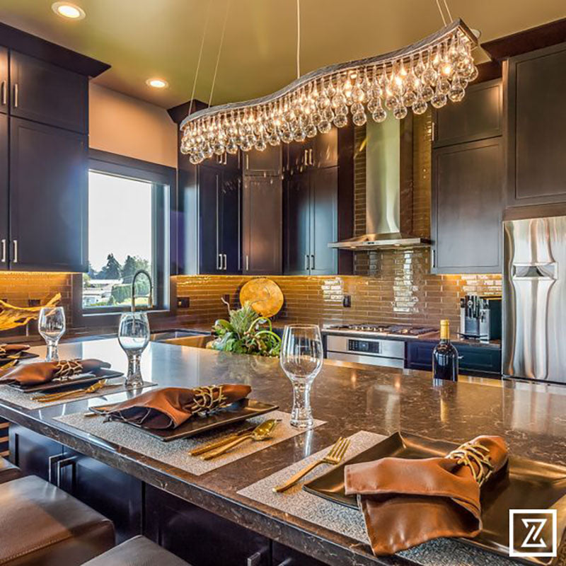 A kitchen island with a granite countertop with dark kitchen cabinets and a large hanging light fixture, all designed by Kate Loeb, Designer at Standard Paint & Flooring. 