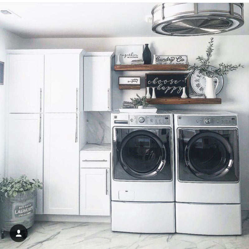 A renovated laundry room by Standard Paint & Flooring, with white storage cabinets and marble tile flooring. 