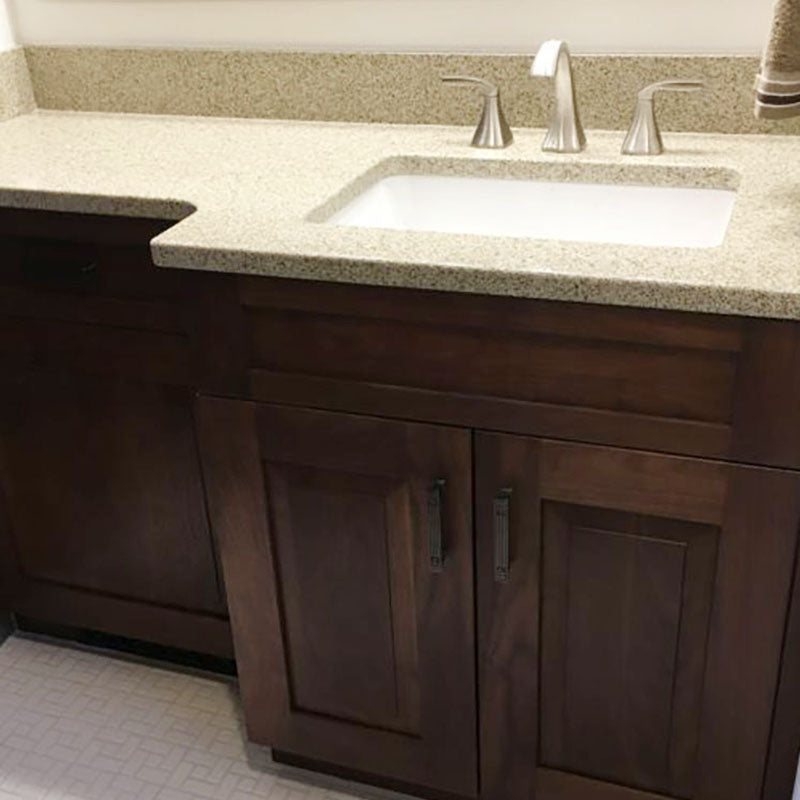A renovated granite bathroom countertop with dark wood cabinets and small white tiled flooring, by Standard Paint & Flooring. 