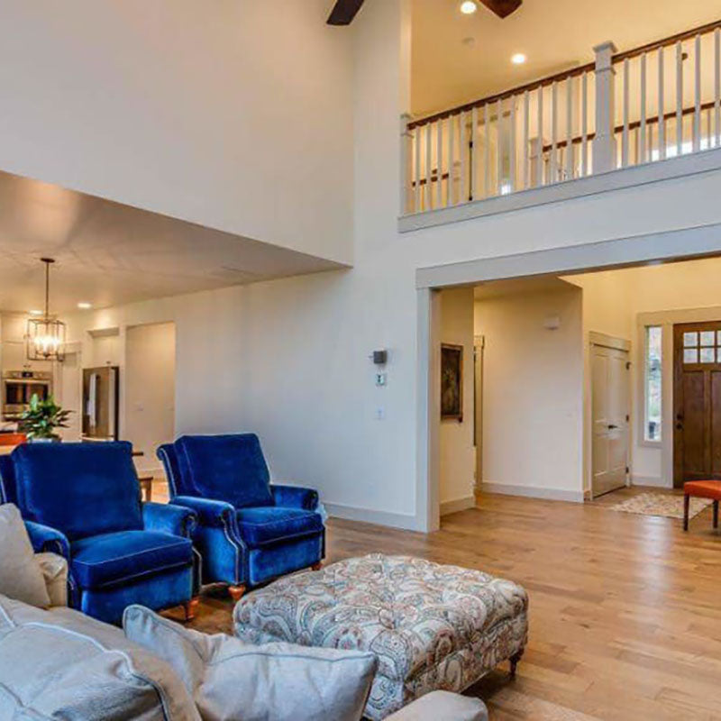 A living room with natural hardwood flooring by Standard Paint & Flooring, showing a kitchen in the back with white cabinets. 