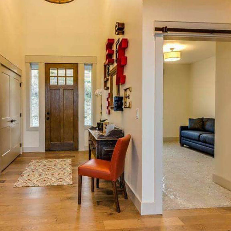 View of an entrance of a home with natural hardwood flooring by Standard Paint & Flooring, a dark wood front door and a patterned carpet.