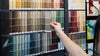 Someone holding a Benjamin Moore paint color chips in front of a wall of paint color chips. 