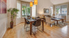 Dining room and living room scene, showing a dark wood dining room table, light grey and white chairs, with large windows and light hardwood flooring. 