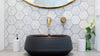 Close up of a black bathroom sink above the counter with small marble white and grey hexagon-shaped wall tile.    