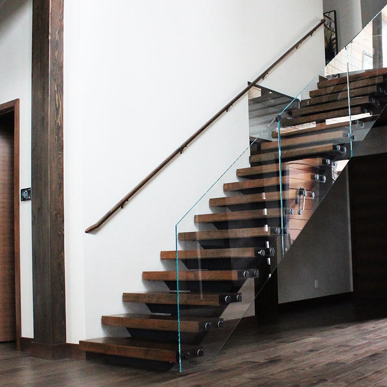 Custom stair case with glass railing, wood banister, and metal detailing by Modern Millwork
