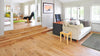 Natural hardwood flooring with a beige couch in front of an office desk and chair, showing open doors to the living room. 