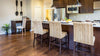 Dark wood laminate flooring in a kitchen, showing a kitchen island with three chairs and a stainless steel fridge and microwave.